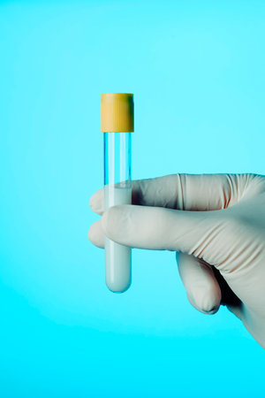closeup of a healthcare worker, wearing white surgical gloves, holding a test tube, in front of a blue backgroundの写真素材