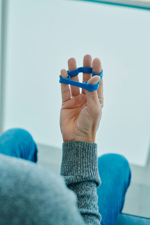 a man uses a blue elastic band to exercise his fingers while is sitting in a chair