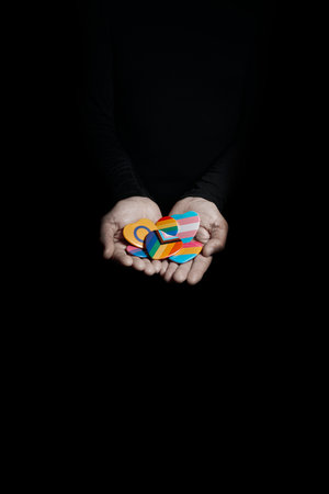 a man holds on his hands some badges with different LGBTQ flags, such as the rainbow flag, the transgender pride flag, or the intersex flag, on a black backgroundの写真素材