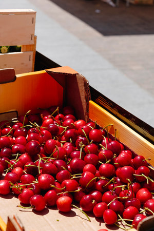 a cardboard crate with some ripe cherries for sale at an open-air market stall on a sunny dayの写真素材