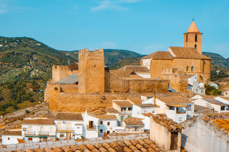 a view of the tiled rooftops of the whitewashed houses in the small town of Iznajar, Spain, built...