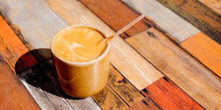 a brown ceramic cup with a french noisette, an espresso with a dash of milk, on the wooden table of an outdoor cafe, in a panoramic format to use as web bannerの写真素材