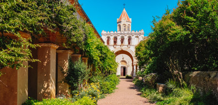 a panoramic view of the entrance courtyard to Lerins Abbey, in Ile Saint-Honorat, France, featuring its beautiful central church and the surrounding vibrant, leafy vegetation, on a sunny spring dayの写真素材