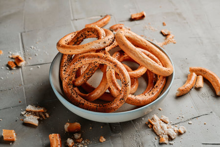 some romanian bread rings, known as covrigi, sprinkled with poppy seeds, on a plate placed on a gray...