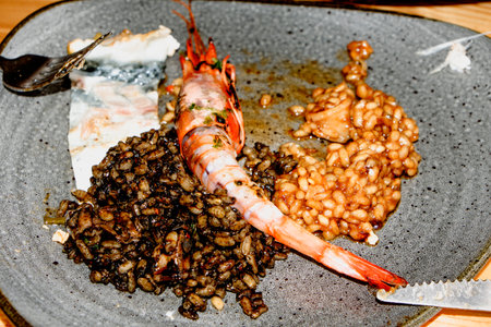 closeup of a gray plate with two kinds of rice, black and reddish, served with a shrimp and a piece of sea bass, on a wooden tableの写真素材