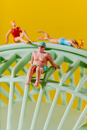 three miniature beachgoers rest and sit across the curved surface of a pale green fan, mimicking a...