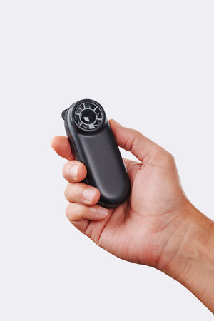 a man cools himself with a compact black battery-powered fan held upright in his hand against a neutral background in a close-up studio shotの写真素材