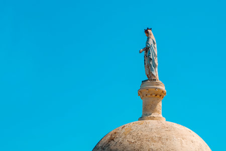 a weathered 19th century statue of the Vierge du Port, the Virgin of the Port, atop a dome on Ile Saint-Honorat in Cannes, France, gazes towards the harbor under a clear blue sky on a sunny spring dayの写真素材