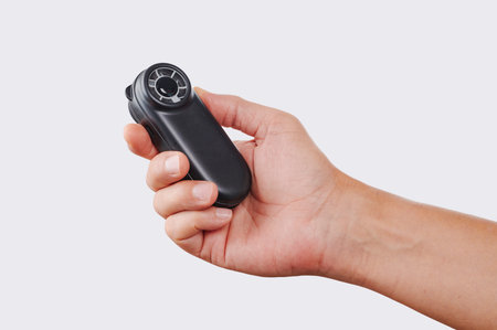 close-up of a person using a small battery-powered handheld fan to refresh themselves while holding it sideways against a plain white studio backgroundの写真素材