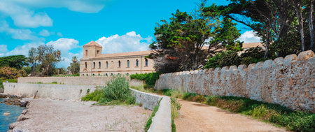 shoreline view of the abbey of Lerins on Ile Saint-Honorat in Cannes, France, its south side and octagonal tower set behind stone walls, with coastal vegetation and the mediterranean sea beside itの写真素材