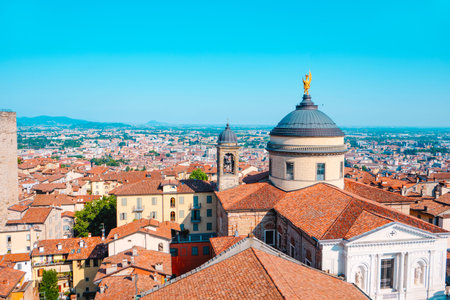 the dome of Sant Alessandro Cathedral with its golden statue stands above the rooftops of the Citta Alta in Bergamo, Italy, as the modern city stretches into the distanceの写真素材