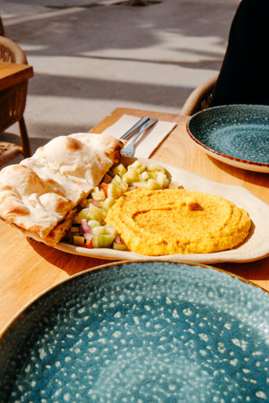 creamy curry hummus served with warm halved naan bread and a colorful fresh salad on a wooden table at a sunny sidewalk cafe surrounded by city lifeの写真素材