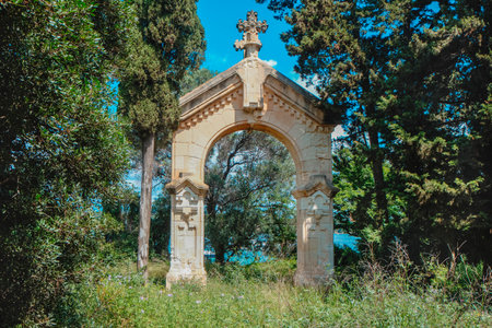at the port entrance to Ile Saint-Honorat, Cannes France, a 19th century triumphal arch topped with a stone cross stands amid cypress and pines with the turquoise sea visible through the trees belowの写真素材