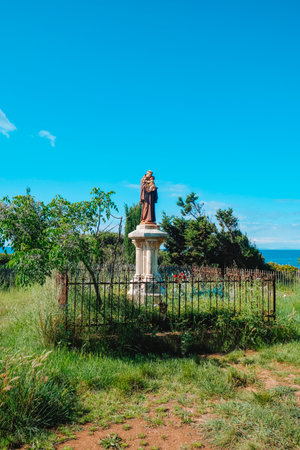 statue of Saint Anthony of Padua holding a child on a stone pedestal, enclosed by a rusty iron fence in a grassy field on Ile Saint-Honorat, Cannes, France, under a clear spring sky near Lerins Abbeyの写真素材