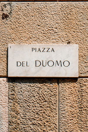a marble street sign reading Piazza del Duomo is mounted on a textured stone wall, marking the central square in front of the Milan Cathedralの写真素材