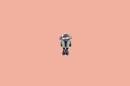 a black and white sad businessman sittin in the floor, curled up, with his head between his knees and his hands in his head, on a pink backgroundの写真素材