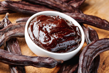 close-up view of rich carob cream in a ceramic bowl placed among whole carob pods on a table, presented as a gluten free alternative to chocolate in Spainの写真素材