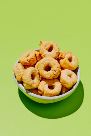 a ceramic bowl containing italian taralli ai semi di finocchio, golden crispy biscuits, traditional savory snack, presented on a bright green surfaceの写真素材