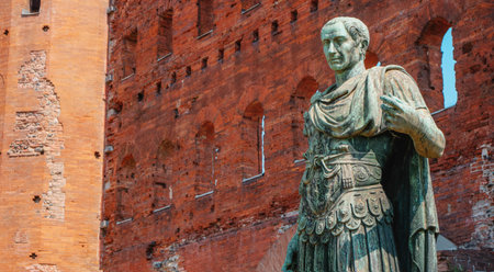 a bronze statue of Caesar Augustus stands before the red brick ruins of Porta Palatina in Turin, Italy, showing the emperor with detailed drapery and armor, framed by ancient wallの写真素材