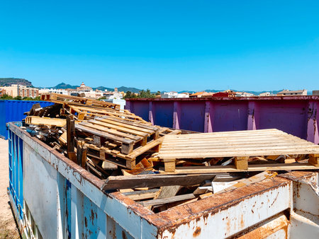 a large open container filled with broken wooden pallets and used wooden planks, located in an outdoor recycling center, with town buildings and mountains visible in the distanceの写真素材