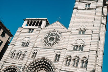 the striped marble facade of the Cathedral of San Lorenzo in Genoa, Italy, rises against a clear blue sky with its rose window and gothic arches in full viewの写真素材