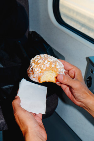 a man holds a brioche con granella di zucchero, a typical Italian sweet pastry topped with coarse sugar, while traveling on a train or bus as daylight streams through the windowの写真素材