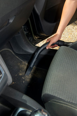 a man cleans the carpet of a car interior using a vacuum nozzle, carefully removing dust and small debris close to the front seat and door area during interior maintenanceの写真素材
