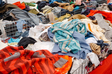 striped shirts and colorful tops are scattered across a full bin of clothing at an outdoor market stall with many garments placed togetherの写真素材