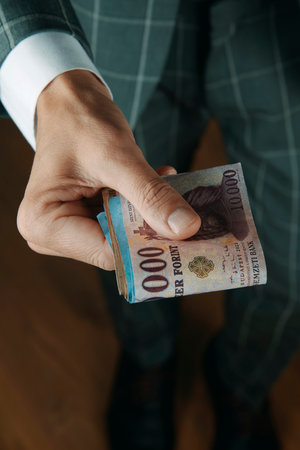 a man in a gray formal suit holding a stack of Hungarian forint banknotes in his hand, symbolizing salary, investment, or financial transactionの写真素材