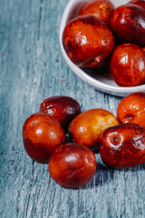 ripe jujube fruits arranged beside a bowl, warm light highlighting their red and amber tones on a cool gray surface, evoking a natural autumn feelの写真素材