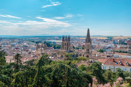 a panoramic view of Burgos, Spain,  shows the cathedral towers rising above the old town rooftops, surrounded by trees and the distant countryside under a clear blue skyの写真素材