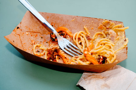 a disposable cardboard box with remaining casarecce alla norma and spaghetti alla carbonara, a fork...