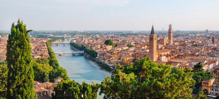 a broad panorama shows the Adige River cutting across Verona, while the Citta Antica rises to the right and the tall bell tower of Sant Anastasia dominates the sunlit skyline above the rooftopsの写真素材