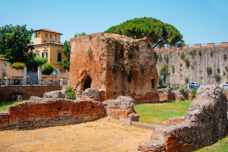 the Bagni di Nerone archaeological remains in Pisa, Italy stand in an outdoor public space, with old brick structures, scattered stones and nearby residential buildings under clear sunlightの写真素材