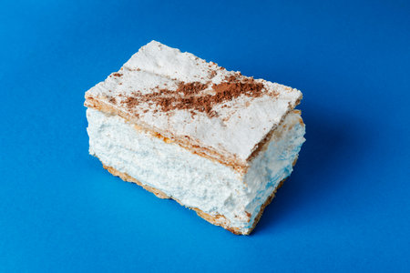 a Spanish milhojas de merengue sits on a blue surface, revealing its generous cloudlike meringue filling and golden puff pastry edges with a dusting of powdered sugar on topの写真素材