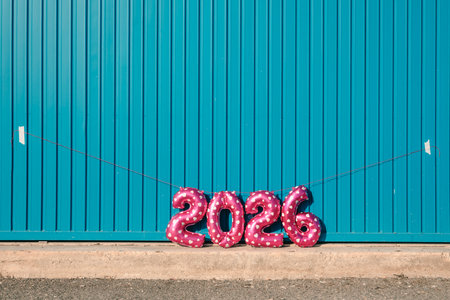 a string of pink balloons forming the number 2026, like the new year, stretches across a wide blue metal wall, creating a playful and colorful compositionの写真素材