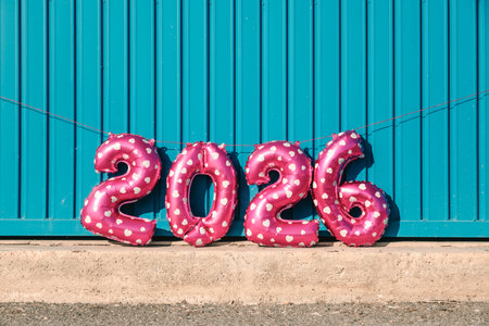 pink heart patterned balloons forming the number 2026, like the new year, rest along a bright blue...