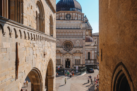 Bergamo, Italy - June 22, 2025: Tourists walk across the stone pavement of Citta Alta while the...