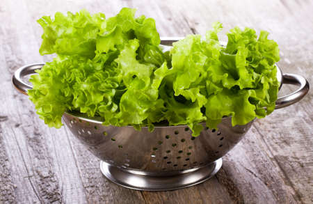 lettuce salad in metal colander on wooden tableの写真素材