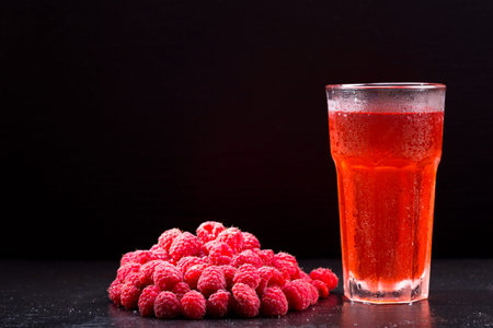 glass of red fruit drink with fresh raspberry over black background