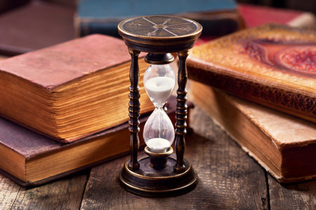 old hourglass with books on wooden background