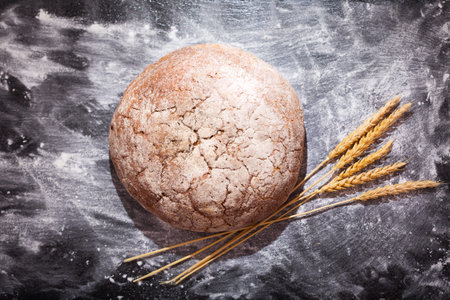 bread with wheat ears on dark board, top view