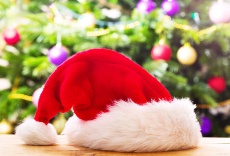 Santa hat on wooden table against christmas tree