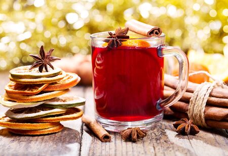 Glass of christmas mulled wine with dried fruit, cinnamon sticks and anise stars on wooden tableの写真素材