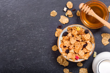 breakfast with cereal flakes, milk and honey on dark background, top view with copy space