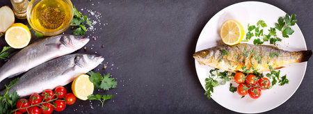 plate of baked sea bass and fresh fish with ingredients for cooking on dark background,top view...