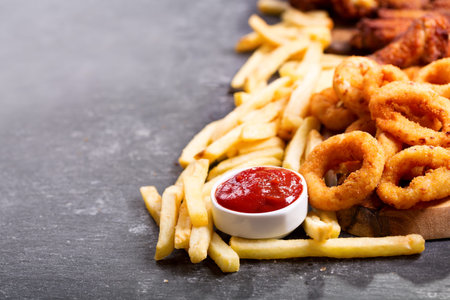 fast food products : onion rings, french fries and fried chicken on dark table