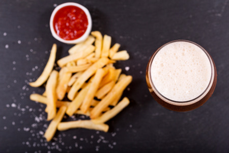 glass of beer with french fries on dark table, top viewの写真素材