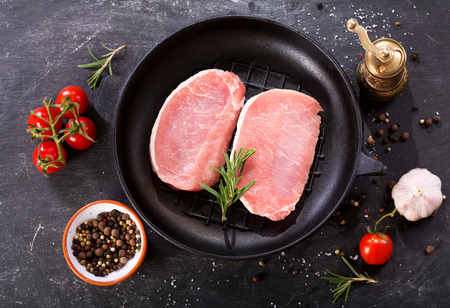 fresh pork in a pan with ingredients for cooking on dark backgroundの写真素材