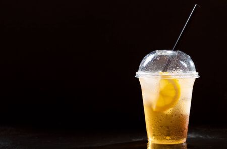 cold iced tea with lemon and straw in takeaway plastic cup on dark backgroundの写真素材
